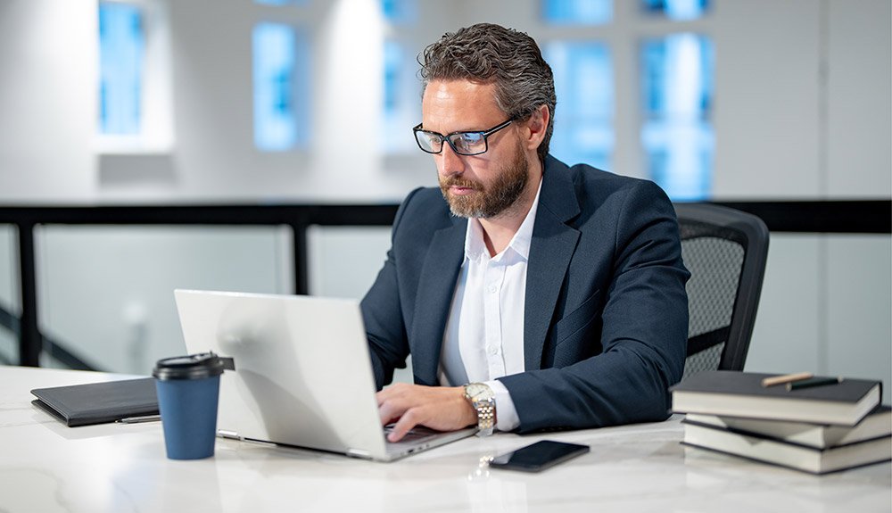 Career change image of bespectacled man searching for jobs on his laptop.